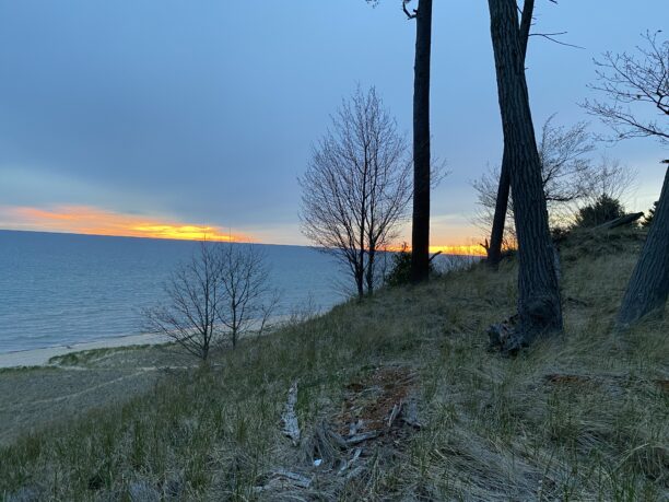 When it comes to cannabis tourism, no trip is compete without a sunset over take Michigan with a bit of orange sky, sand dunes and bare trees near the beach