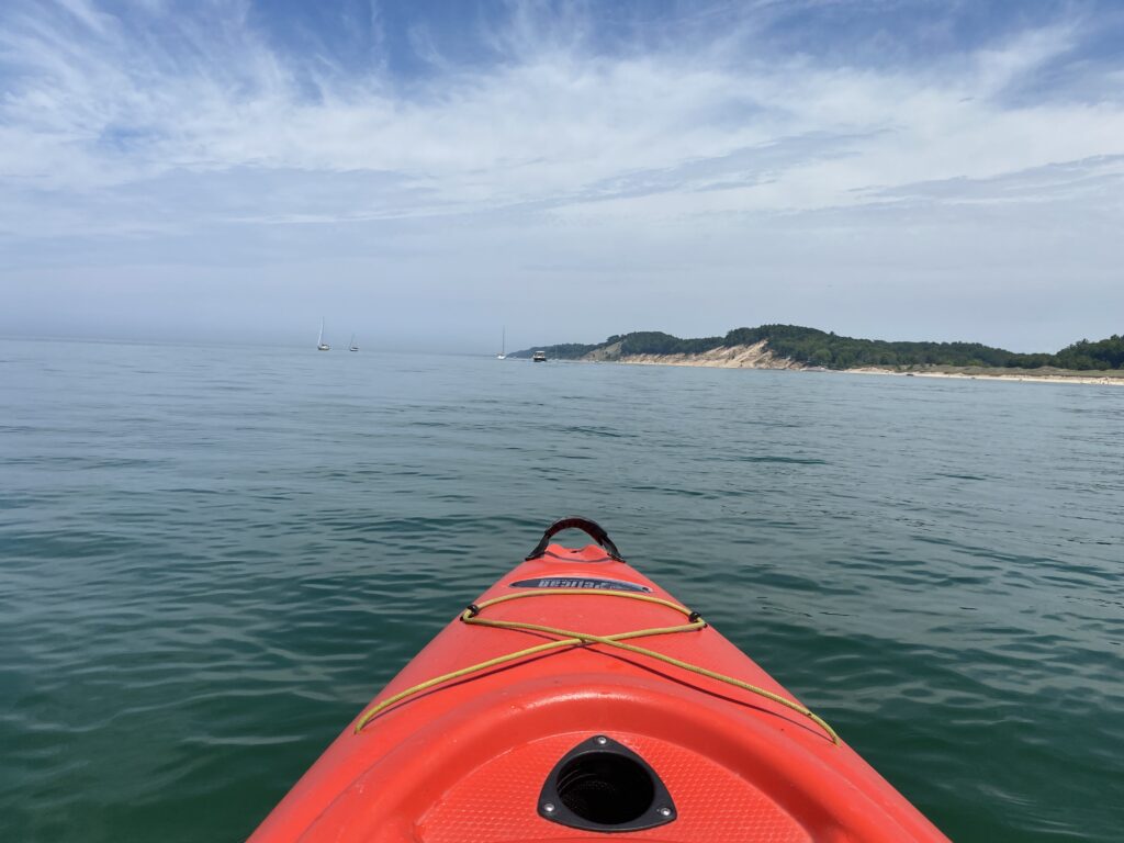 cannabis tourism in Michigan is one the rise and this image shows a red kayak in blue water  and the shore of Lake Michigan